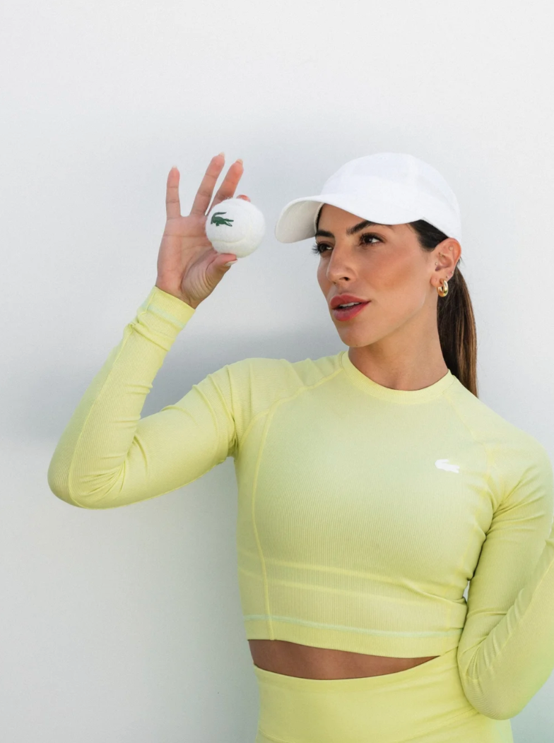 Woman in a yellow activewear set holding a tennis ball, brand campaign still by Leo R.