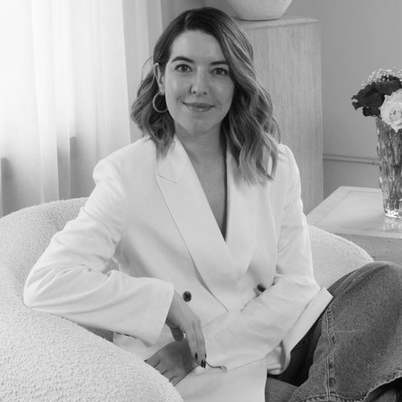 Professional woman in a white blazer seated in a bright, modern room