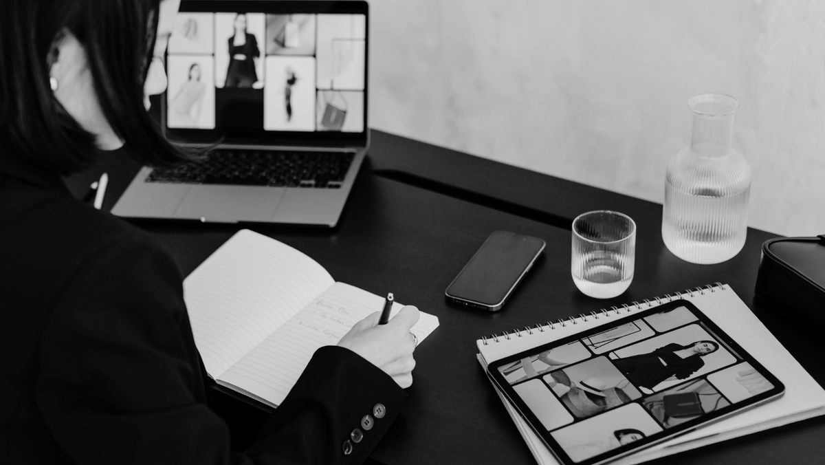 Woman working at a desk with a laptop, notebook and printed design layouts