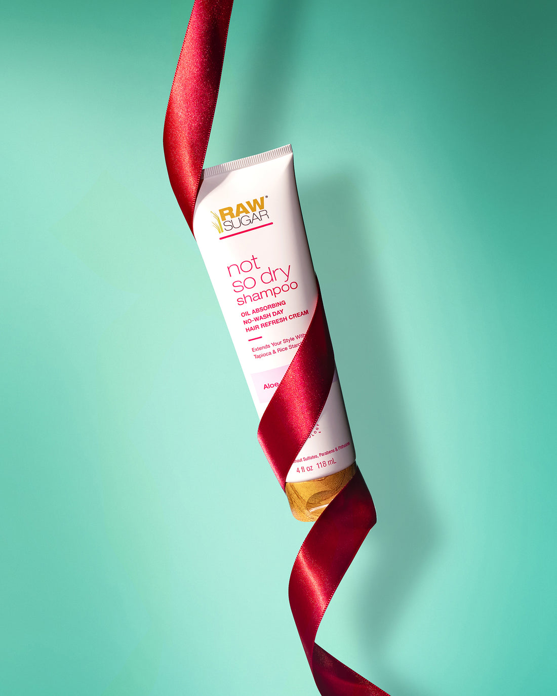 Hand cream tube wrapped in red ribbon on a teal background, product photography by Melissa E.