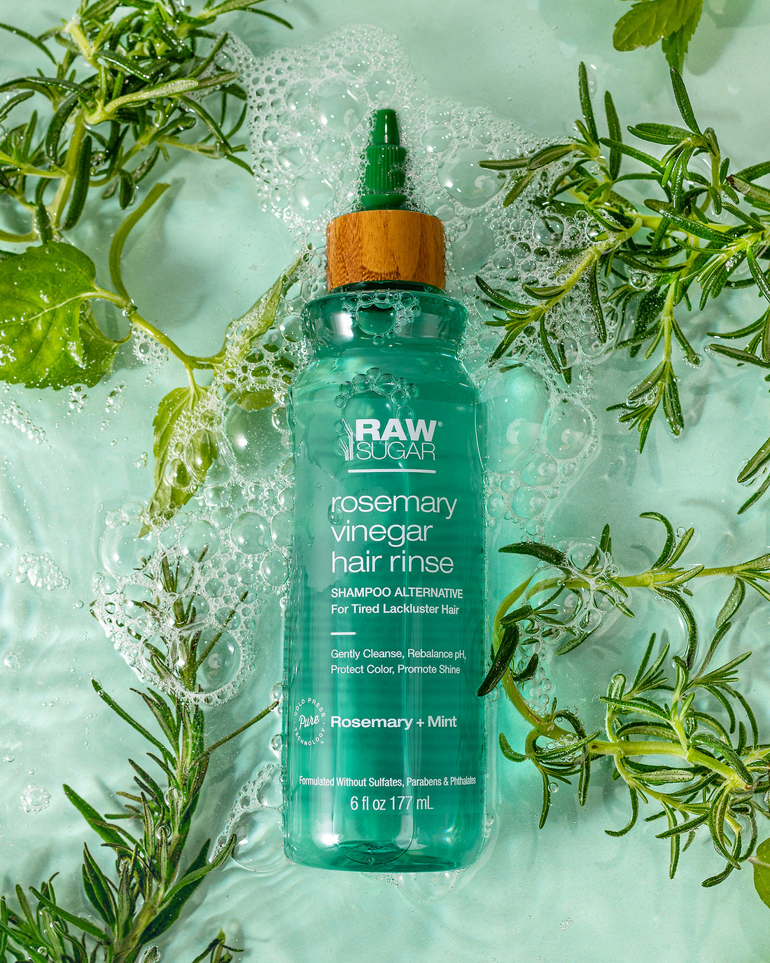 Green hair rinse bottle surrounded by herbs and water, product photography by Melissa E.