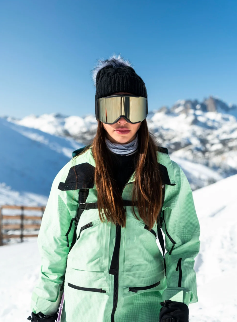 Woman in a mint ski jacket on a snowy mountain, brand campaign still by Leo R.